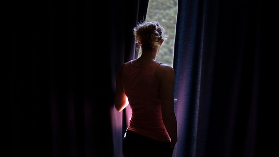 Frau schaut durch Vorhaenge aus einem Fenster © picture alliance / photothek Foto: Ute Grabowsky