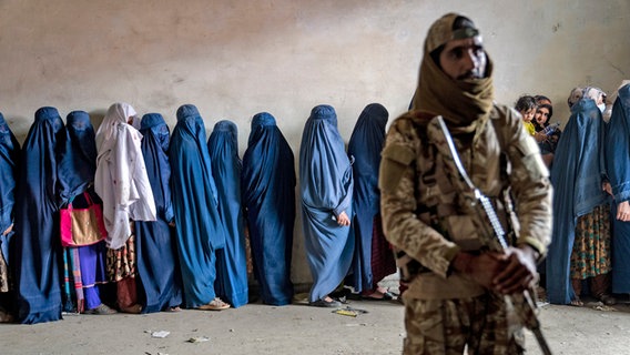 In blauem Stoff (Burka) verhüllte Frauen warten in Kabul in einer Schlange, um von einer humanitären Hilfsorganisation verteilte Lebensmittelrationen zu erhalten © Ebrahim Noroozi/AP/dpa +++ dpa-Bildfunk +++ Foto: Ebrahim Noroozi