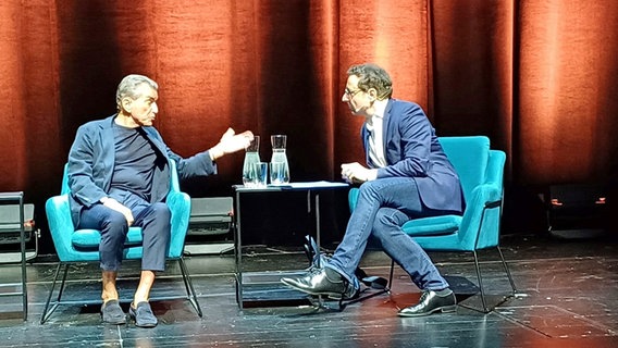 Michel Friedman und Ulrich Kühn sitzen im Gespräch auf Sesseln auf einer Bühne und schauen sich an. © NDR Foto: Alexander Solloch