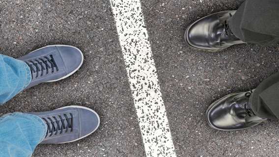 Zwei Fußpaare stehen sich gegenüber, getrennt durch eine weiße Linie © picture alliance / Zoonar | DesignIt 