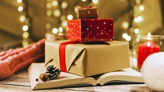 Ein Buch und weitere eingepackte Geschenke liegen vor einem Weihnachtsbaum © picture alliance / Zoonar | Oleksandr Latkun 