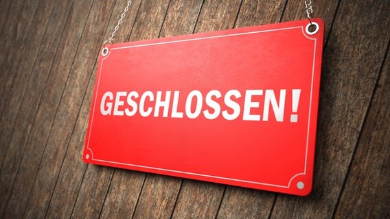 Ein rotes Schild mit der weißen Aufschrift "geschlossen" hängt vor einer Holzwand. © picture alliance / Zoonar | Alexander Limbach 