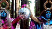 Zwei phantasievoll gekleidete und geschminkte Menschen halten ein glitzernde Diskokugel zwischen sich - ein Videostill "Style over Substance" von The Huxleys. © The Huxleys 
