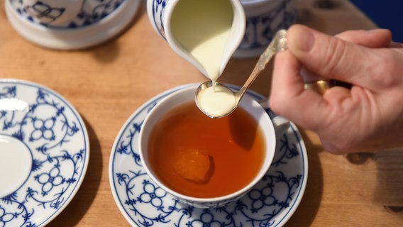 Aus einem Kännchen wird Sahne auf einen Teelöffel gegossen, der über einer blau-weißen Teetasse gehalten wird. © picture alliance / dpa Foto: Carmen Jaspersen
