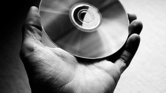 Schwarz-Weiß-Fotografie einer linken Hand die eine CD hält. © ***DJ*** / photocase.de Foto: ***DJ***