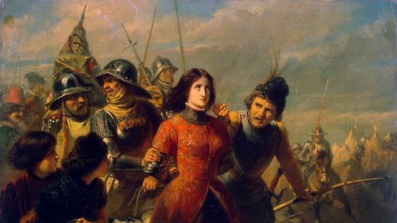 Auf einem Gemälde sieht man eine Frau in rotem Kleid, die von Soldaten festgenommen wird. Ihr Blick geht starr zum Himmel. Sie wirkt gedanklich abwesend. © IMAGO / Heritage Images Foto: IMAGO / Heritage Images