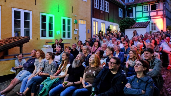 Eine Gruppe von Menschen sitzt in einem Hinterhof in Flensburg auf Stühlen und freut sich. © Flensburger Hofkultur 