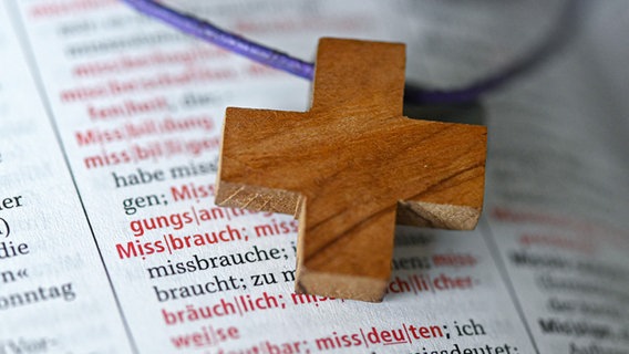 Ein Holzkreuz liegt neben dem Wörterbucheintrag "Missbrauch" © picture alliance / epd-bild | Foto: Heike Lyding