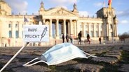Ein Mund-Nasen-Schutz und ein Schild mit der Aufschrift "Impfpflicht" vor dem Deutschen Bundestag © picture alliance / Flashpic Foto: Jens Krick