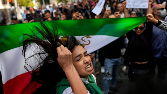 Eine Frau ruft Parolen neben einer iranischen Fahne während einer Demonstration vor der iranischen Botschaft nach dem Tod der Iranerin Mahsa Amini. © picture alliance/dpa/AP Foto: Francisco Seco