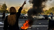 Eine Frau steht während einer Demonstration in Teheran vor einem brennenden Autoreifen und zeigt das Victory-Zeichen. © Uncredited/AP/dpa 