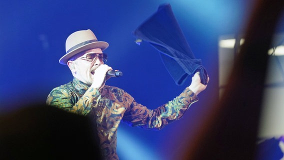 Jan Delay singt auf einer Bühne in ein Mikrofon und schwingt dabei ein Handtuch. © picture alliance/dpa | Marcus Brandt 