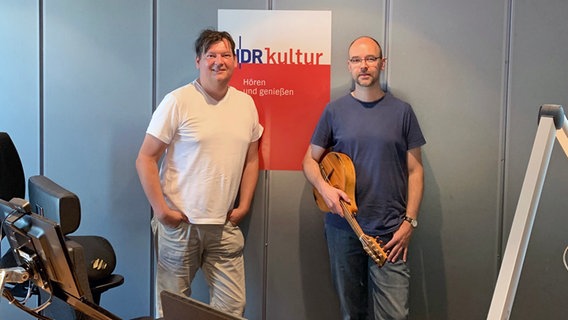 Der Mandolinist Jochen Roß hält sein Instrument und steht neben Moderator Philipp Schmid im Studio von NDR Kultur. © NDR Foto: Nora Schmidtke