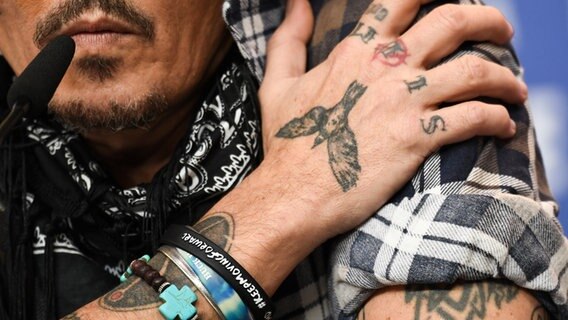 Eine Nahaufnahme von Johnny Depps Armen und rechter Hand während ein Pressekonferenz zeigt seine Tattoos. © picture alliance/dpa/Sputnik | Ekaterina Chesnokova 