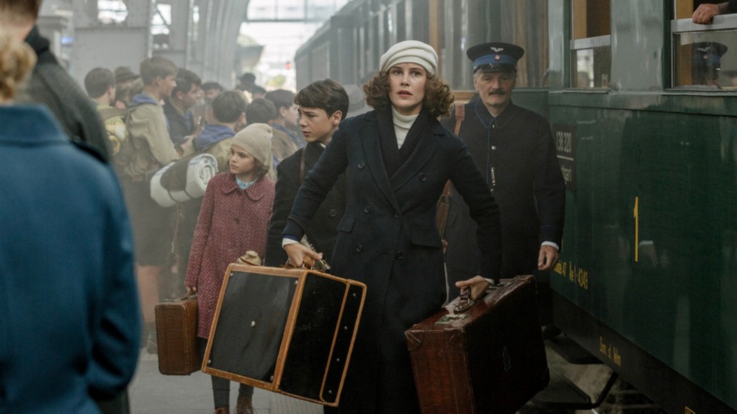 Dorothea (Carla Juri) und ihre Kinder Anna (Riva Krymalowski) und Max (Marinus Hohmann) gehen auf einem vollen Bahnsteig an einem Zug vorbei.