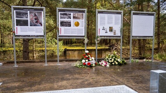 Blumenkränze liegen vor vier Schautafeln, die vor einem Wald stehen © picture alliance/dpa Foto: Stefan Sauer