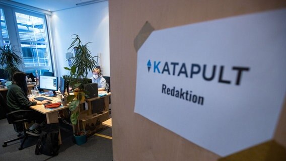 Durch eine offene Tür mit dem Schild "Katapult Redaktion" sind an PCs arbeitende Menschen in einem Raum zu sehen. © picture alliance/dpa/dpa-Zentralbild Foto: Jens Büttner