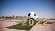 Ein großer Ball mit der Jahreszahl 2022 steht auf einer Verkehrsinsel mit Kreisverkehr vor dem Trainigsgelände Al-Shamal sports Club in der Hafenstadt Al Ruwais. © picture alliance/dpa Foto: Christian Charisius