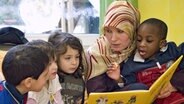 Eine muslimische Kindergärtnerin liest Kindern aus einem Buch vor. © imago 