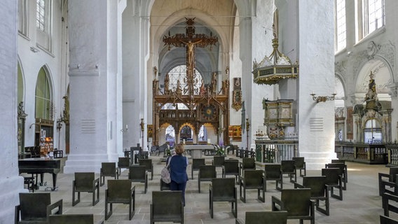 Der Innenraum des Lübecker Doms, zwischen leeren Stuhlreihen steht eine Frau. © picture alliance / Zoonar | Achim Prill 