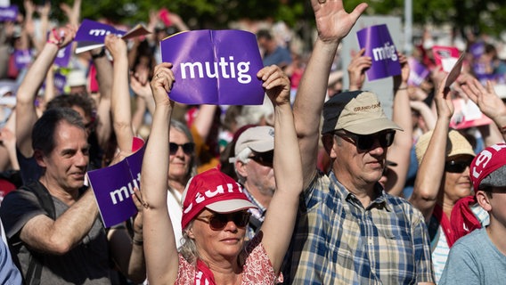 Eine Frau hält bei einer Veranstaltung im Freien beim Kirchentag 2025 in Hannover ein Schild hoch mit der Aufschrift "mutig". © dpa Foto: Moritz Frankenberg