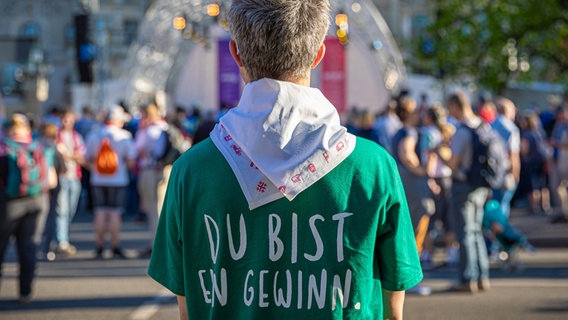 Ein Mann mit einem grünen T-Shirt mit der Aufschrift auf dem Rücken "Du bist ein Gewinn" - bei der Eröffnung des 39. Evangelischen Kirchentages in Hannover. © dpa Foto: Moritz Frankenberg