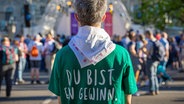 Ein Mann mit einem grünen T-Shirt mit der Aufschrift auf dem Rücken "Du bist ein Gewinn" - bei der Eröffnung des 39. Evangelischen Kirchentages in Hannover. © dpa Foto: Moritz Frankenberg