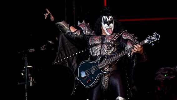 Gene Simmons, der Bassist von KISS, reckt bei einem auftritt den rechten Arm hoch und streckt seine Zunge aus. © picture alliance / Photoshot 