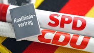 Zwei Stifte mit der Aufschrift SPD und CDU, dazu ein kleines graues Büchlein mit dem Schriftzug Koalitionsvertrag. © picture alliance / CHROMORANGE Foto: Christian Ohde