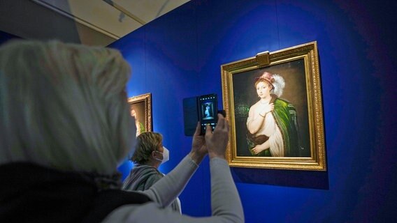Besucher fotografieren und betrachten das Kunstwerk "Junge Frau mit Federhut" von Tizian, das dem Eremitage-Museum gehört, in der Gallerie d'Italia. © picture alliance/dpa/AP | Luca Bruno 