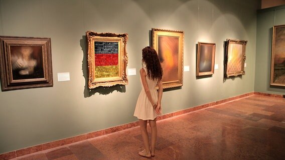 Eine Frau schaut sich in einer Kunstausstellung ein Bild in schwarz-rot-gold-Optik an (Bildmontage) © Fotolia Foto: andreas130, JiSIGN