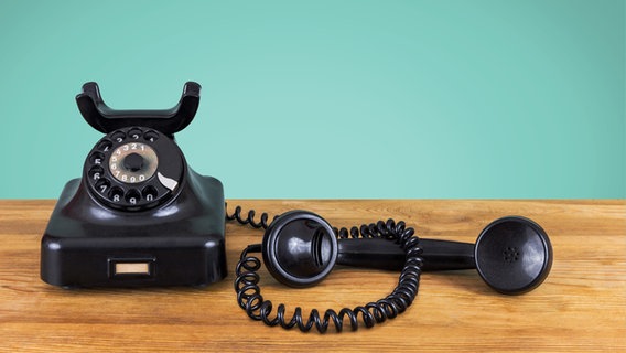Ein altes Telefon steht auf einer Holzfläche, der Hörer ist abgenommen. © photocase Foto: pixelklex