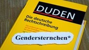 Auf einem Duden liegt ein Stück ausgerissendes Papier, auf dem "Gendersternchen*" steht. © picture alliance/dpa-Zentralbild Foto: Sascha Steinach