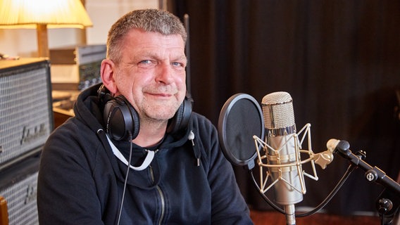 Jörn Menge sitzt in einem Tonstudio vor einem Mikrofon und trägt Kopfhörer. © picture alliance/dpa Foto: Georg Wendt