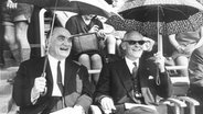 Ein Schwarz-Weiß-Foto mit zwei lachenden Männern, die aufgespannte Regenschirme halten. (Bischof Kurt Scharf (l) und Willem Visser't Hooft, ehemaliger Generalsekretär des Weltkirchenrates) © picture-alliance / dpa Foto: Wolfgang Weihs