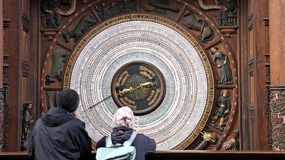 Zwei Menschen stehen auf der Empore der Rostocker Marienkirche und bewundern die 550 Jahre alte astronomische Uhr © Bernd Wüstneck/dpa +++ dpa-Bildfunk Foto: Bernd Wüstneck