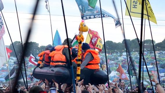 Schlauchboot mit als Flüchtlinge gestalteten Puppen über den Köpfen der Zuschauer auf einem Konzert. © picture alliance / Cover Images | CelebrityPhotosUK/Cover Images 