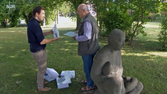 Der Historiker Jakob Schwichtenberg zeigt Wolfgang Pfannenschmidt einen Entwurf für die Plastik von Bützow, während sie neben dem Original stehen. © NDR 