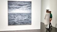 Auf einer weißen Wand hängt ein Bild vom Meer, zwei Frauen gehen daran vorbei © Georg Wendt/dpa Foto: Georg Wendt