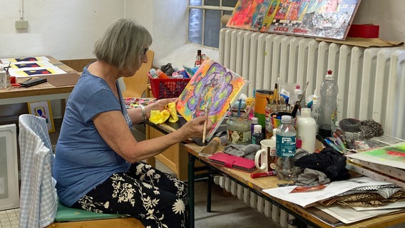 Frau sitzt an einer Tischstaffelei in der Räumen des Künstlerkollektives "Kunst in der Klinik" © NDR.de Foto: Antonia Reiff
