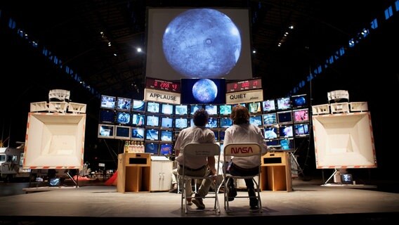 Zwei Menschen sitzen auf Stühlen vor einer Installation, die wie ein Raumfahrt-Kontrollzentrum aussieht. © Tom Sachs Foto: Genevieve Hanson