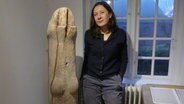 Ein großer Holzstamm, der die Form eines Phallus hat, rechts neben ihr steht eine Frau. © Peter Bartelt / NDR Foto: Peter Bartelt