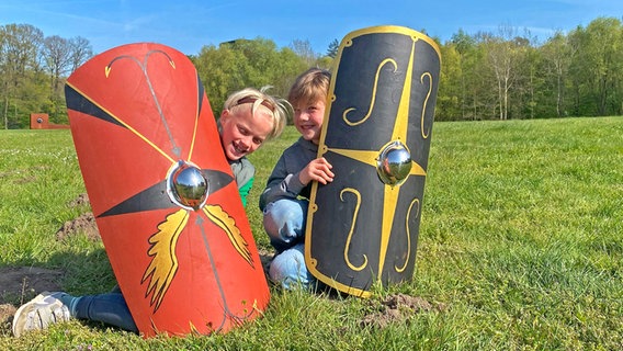 Zwei Kinder spielen auf der Wiese mit riesigen Schildern wie zur Ritterzeit im Museum Kalkriese © Museum Kalkriese 