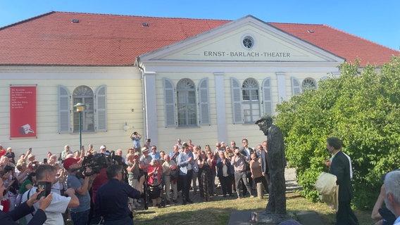 Eine Menschenmenge vor einem Theater, in der Mitte eine Statue eines leicht nach vorn gebeugten Mannes. © Golo Schmiedt Foto: Golo Schmiedt