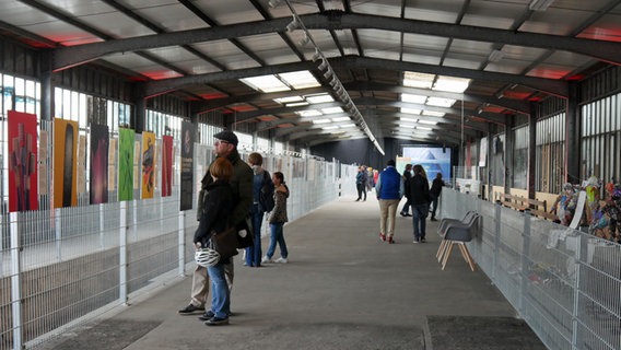 Besucher gucken sich in einer Halle Bilder der Ausstellung "Planet or Plastic?" an. © NDR 