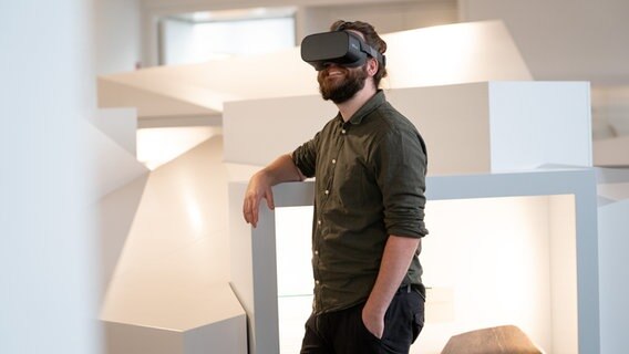 Ein Mann mit Virtual Reality-Brille steht an einer Skulptur und lächelt. © Museum Lüneburg 