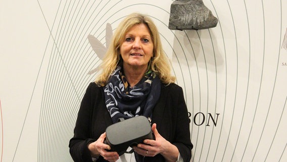 Eine Frau mit blonden schulterlangen Haaren hält eine Virtual-Reality Brille in den Händen. Eine Frau mit blonden schulterlangen Haaren hält eine Virtual-Reality Brille in den Händen. © Museum Lüneburg