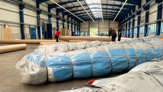Ein dickes blaues Bündel Stoff, eingepackt in eine Kunststoffhülle, liegt in einer großen Werkhalle. © NDR Foto: JW