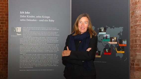 Eine Frau steht lächelnd und mit verschränkten Armen vor einer Ausstellungswand. © Franziska Taffelt / Save the Children Foto: Franziska Taffelt