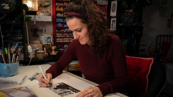 Die Künstlerin Julie Weißbach sitzt an einem Tisch und zeichnet. © NDR Foto: Linda Ebener